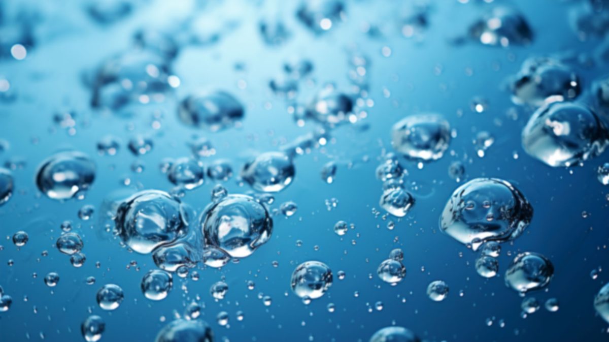 Primer plano de numerosas pequeñas burbujas de aire suspendidas en un líquido azul transparente que recuerda al agua hidrogenada. Las burbujas varían de tamaño y captan y reflejan la luz, creando un efecto brillante contra el fondo liso.