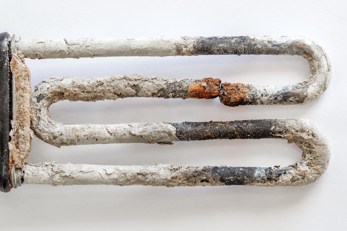 Primer plano de un elemento calefactor corroído y con abundantes incrustaciones sobre un fondo blanco. El metal está oxidado y cubierto de depósitos minerales blancos, lo que resalta el desgaste y el deterioro.