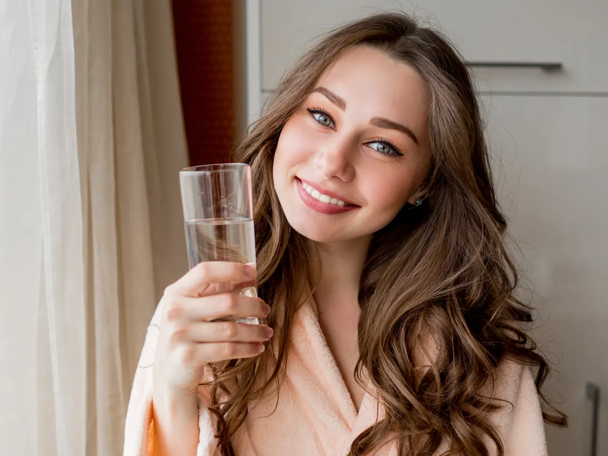 Mujer sonriente bebiendo un vaso de agua en casa